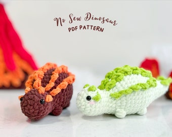 May include: Two crocheted dinosaur toys, one brown with orange spikes and one white with green spikes. The toys are sitting on a white surface. The text "No Sew Dinosaur PDF PATTERN" is written above the toys.