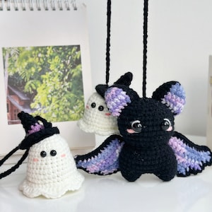 May include: Two crocheted Halloween ornaments, a white ghost wearing a black witch hat and a black bat with purple and blue wings.