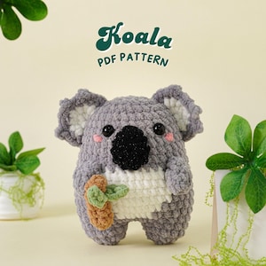 Puede incluir: Un juguete de peluche de koala tejido a crochet que sostiene una pequeña zanahoria tejida a crochet. El koala es gris y blanco con ojos negros y una nariz negra. El texto "Koala PDF Pattern" está encima del juguete.