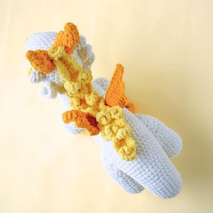 May include: A white crocheted unicorn toy with yellow and orange crocheted wings and mane.