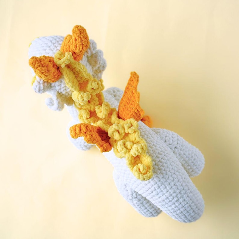 May include: A white crocheted unicorn toy with yellow and orange crocheted wings and mane.
