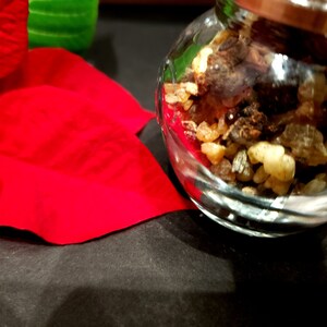May include: A glass jar filled with a mixture of brown and light brown resin pieces. The jar is sitting on a black surface.