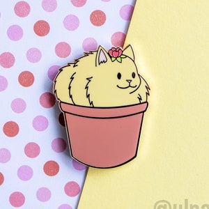 May include: A yellow cat with a flower crown is sitting in a pink flower pot. The cat is looking to the right. The background is a pink and white polka dot pattern.