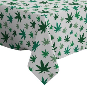 Puede incluir: Un mantel blanco con un patrón repetido de hojas verdes de marihuana.