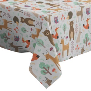 May include: A white tablecloth with a woodland animal print. The print features deer, bears, owls, foxes, and mushrooms in shades of brown, orange, green, and purple.
