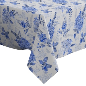 Può includere: Una tovaglia bianca con un motivo floreale blu. La tovaglia presenta un motivo ripetitivo di fiori blu e foglie su uno sfondo bianco.