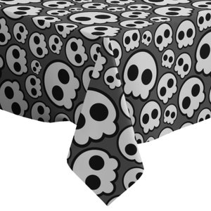 Pode incluir: Toalha de mesa preta e branca com um padrão de caveiras. As caveiras são de vários tamanhos e são delineadas em branco. O fundo é cinza escuro.