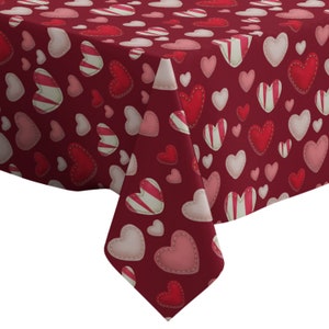 Könnte beinhalten: Eine bordeauxfarbene Tischdecke mit einem sich wiederholenden Muster aus Herzen in verschiedenen Größen und Stilen. Die Herzen sind in Rot-, Rosa- und Weißtönen gehalten, einige mit Streifenmustern. Die Tischdecke ist gefaltet.