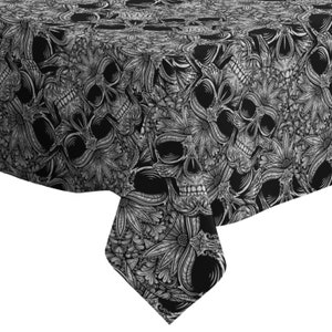 Op de afbeelding: Zwart-witte tafelkleed met een schedel- en bloemenpatroon. Het tafelkleed is gemaakt van een zachte, duurzame stof en is perfect om een ​​toets van gotische elegantie aan uw eetkamer toe te voegen.
