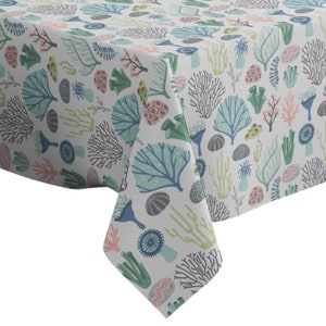Może przedstawiać: Biały obrus z powtarzającym się wzorem kolorowych koralowców i życia morskiego. Wzór zawiera niebieskie, zielone, różowe i szare koralowce, jeżowce i inne elementy morskie. Obrus jest wykonany z wytrzymałej tkaniny.