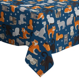 May include: A blue tablecloth with a repeating pattern of orange, gray, and white cats. The cats are in various poses, including sitting, standing, and lying down. The tablecloth has a paw print pattern.