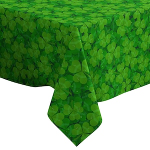 May include: A green tablecloth featuring a repeating pattern of shamrocks. The shamrocks are in varying shades of green, with some appearing to have water droplets. The tablecloth is folded over a surface.