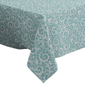 Peut inclure: Une nappe turquoise avec un motif floral blanc. La nappe a un design damassé avec des feuilles et des fleurs en spirale.
