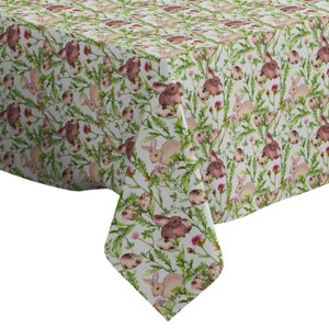 Pode incluir: Toalha de mesa branca com um padrão repetido de coelhos marrons e rosados, folhas verdes e ovos salpicados.