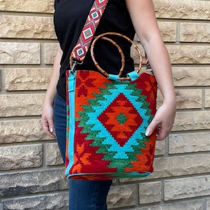 May include: A large, colorful tote bag with a geometric pattern in shades of red, orange, blue, and green. The bag has a wooden handle and a long strap with a geometric pattern.