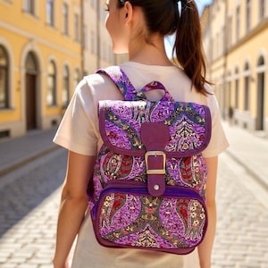 May include: A purple paisley patterned backpack with a flap closure and a buckle. The backpack has a front pocket and adjustable straps. The bag is made of a patterned fabric with shades of purple, red, and gold.