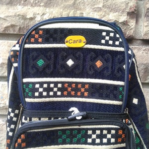 May include: A blue and white patterned backpack with a yellow name tag that says "Cara".