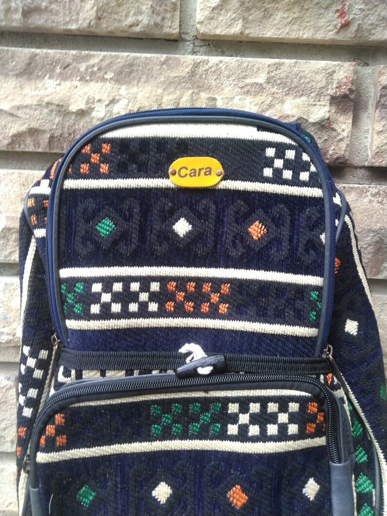 May include: A blue and white patterned backpack with a yellow name tag that says "Cara".