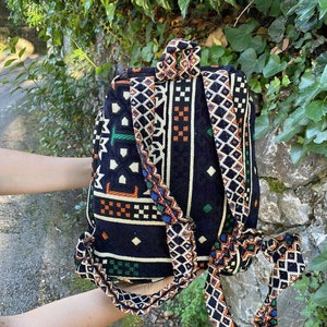 May include: A black backpack with a colorful geometric pattern. The straps are made of the same fabric as the bag and have a woven design.