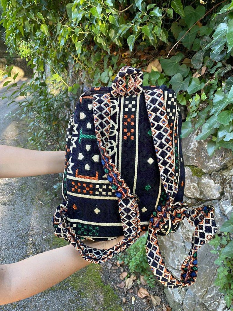 May include: A black backpack with a colorful geometric pattern. The straps are made of the same fabric as the bag and have a woven design.