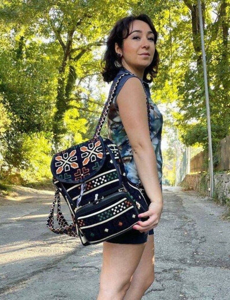 May include: A black and white patterned backpack with a flap closure and a small front pocket. The backpack has a geometric design with orange and green accents.