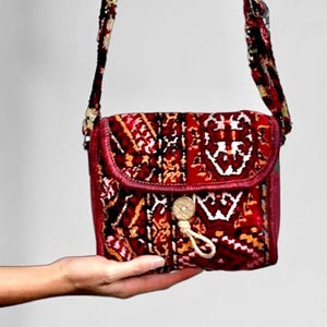 May include: A small red crossbody bag with a colorful patterned design. The bag has a flap closure and a decorative button.