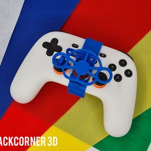 May include: A white video game controller with a blue and orange fan attached to it. The controller is on a multi-coloured background.