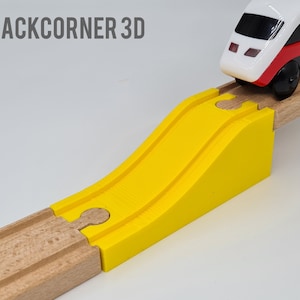 Op de afbeelding: Een gele plastic treinbaanhelling verbindt met een houten treinbaan. De helling is ontworpen om een ​​speelgoedtrein naar een hoger niveau van de baan te laten rijden.