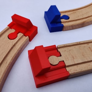 Op de afbeelding: Drie houten treinbaanstukken met rode en blauwe plastic connectoren. De connectoren hebben een puzzel-achtig ontwerp.