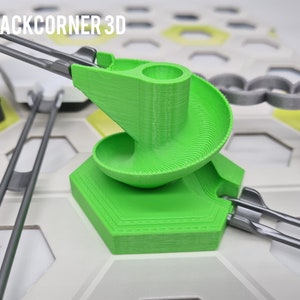 Könnte beinhalten: Ein grünes, 3D-gedrucktes Spiralbahnstück für ein Murmelbahn-Spiel. Die Bahn ist an einer sechseckigen Basis befestigt und hat eine graue Metallbahn, die daran befestigt ist.