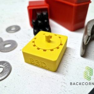 Puede incluir: Un engranaje amarillo impreso en 3D con una peque&ntilde;a perilla en la parte superior. El engranaje tiene las letras "B3D" impresas en el lateral.
