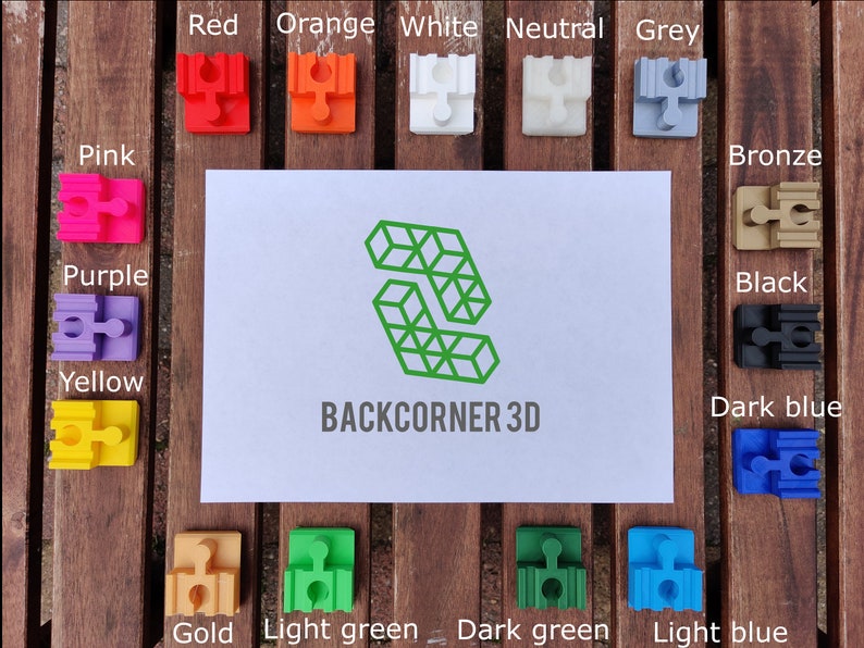 Puede incluir: Una colecci&oacute;n de 14 peque&ntilde;as piezas de rompecabezas de pl&aacute;stico en varios colores, incluyendo rojo, naranja, blanco, neutro, gris, rosa, morado, amarillo, bronce, negro, azul oscuro, dorado, verde claro, verde oscuro y azul claro. Las piezas est&aacute;n dispuestas en dos filas sobre una superficie de madera. El texto "BACKCORNER 3D" est&aacute; impreso en una tarjeta blanca en el centro de la imagen.