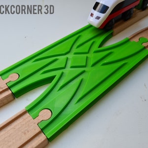 May include: A green plastic train track switch connects to two wooden train tracks. A white and red toy train is on the track.