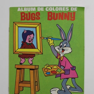 May include: A green colouring book cover featuring Bugs Bunny painting a picture of a pig in a frame. The title of the book is "Album de Colores de Bugs Bunny".