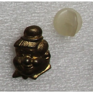 Puede incluir: Una figurita de metal de color dorado que representa a una persona con un sombrero. La figurita está sentada con las piernas cruzadas. La figurita mide aproximadamente 5 cm de alto.