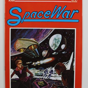 Könnte beinhalten: Ein roter Atari SpaceWar-Spielekarton mit einem blau-weißen Titel und einer Weltraumszene mit Planeten, Sternen und Raumschiffen. Das Cover zeigt zwei Personen im Vordergrund, eine trägt eine Sonnenbrille und die andere schaut auf ein Bedienfeld.