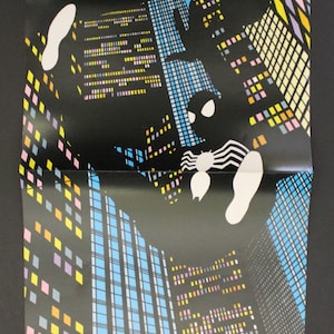 May include: A black and white illustration of Spider-Man hanging upside down in front of a city skyline. The buildings are made up of colourful squares and rectangles.