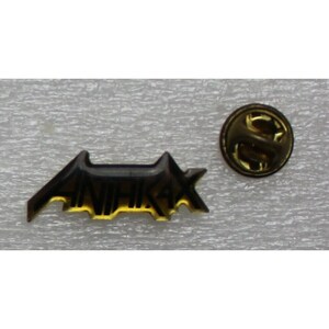 May include: A gold-colored pin with the word "ANNIHILAX" in black lettering. The pin has a safety clasp on the back.