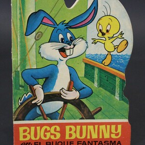 May include: A vintage Bugs Bunny book cover featuring Bugs Bunny steering a ship's wheel with Tweety Bird standing on the railing. The cover is red, yellow, and blue with the title "Bugs Bunny en el Buque Fantasma".