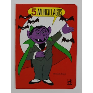 May include: A vintage children's book cover featuring a cartoon vampire character with purple skin, a black beard, and a green cape. The title "5 Murcielagos" is displayed above the character, with bats in the background.