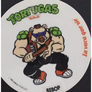 Op de afbeelding: Een ronde witte sticker met een cartoon afbeelding van Bebop, een personage uit de Teenage Mutant Ninja Turtles franchise. Bebop is een varkenachtige humanoïde die een zonnebril, een vest en een bruine riem draagt. Hij houdt een stok in zijn rechterhand en heeft een groene schildpad op zijn linker schouder. De sticker heeft de tekst "Tortugas Ninja" bovenaan en "La vaca que rie" rechts. De tekst "Bebop" staat onderaan de sticker.