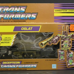 Puede incluir: Un robot de juguete Transformers verde y negro, Oslat, en modo vehículo. El juguete es un líder Combaticon Decepticon y puede combinarse con otros juguetes Combaticon para formar Bruticus. La caja es dorada con acentos morados y amarillos. El texto en la caja dice "Transformers" y "Combaticon Leader".