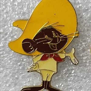 Op de afbeelding: Een kleurrijke emaille pin met een cartoonmuis met een gele sombrero, een rode vlinderdas en een crèmekleurige outfit. De muis heeft bruine vacht en lacht. De pin is een verzamelobject.