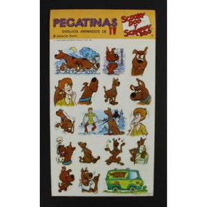 May include: A sheet of vintage Scooby-Doo and Scrappy-Doo stickers. The stickers feature various cartoon images of Scooby-Doo, Shaggy, and the Mystery Machine van. The sticker sheet has text in Spanish.