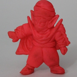 May include: A bright pink plastic figurine of a cartoon character with a pointed hat and a long, flowing cape. The character has large eyes and a wide mouth.