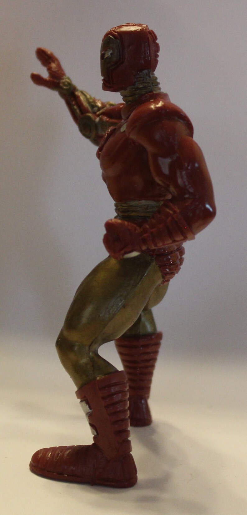 May include: A red and gold action figure of a superhero with a raised arm and a closed fist. The figure is posed in a dynamic stance with one leg forward and the other leg back. The figure has a detailed sculpt and paint job.