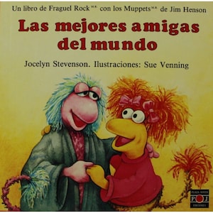 Op de afbeelding: Een kinderboekomslag met twee Muppet-personages, een roze en blauwe Fraggle en een geel en rood vogelachtig personage. De titel van het boek is "Las mejores amigas del mundo" en de auteur is Jocelyn Stevenson. Het boek is geïllustreerd door Sue Venning.