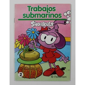 Puede incluir: Un personaje de dibujos animados rosa y morado con un vestido rojo y una flor en la mano. El personaje está de pie sobre una base con estampado amarillo y naranja. La portada del libro tiene el título "Trabajos submarinos" y la palabra "Snorkels" en una burbuja. El libro es el número 2 de una serie y está publicado por Parramón.