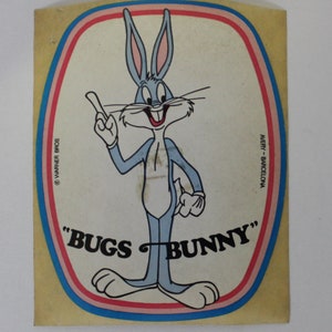May include: A vintage sticker featuring Bugs Bunny, a cartoon rabbit, with a blue and white colour scheme. The sticker has a yellow background with red, blue, and white borders. The text "Bugs Bunny" is printed in black letters on the sticker. The sticker is from Avery - Barcelona and is copyrighted by Warner Bros.