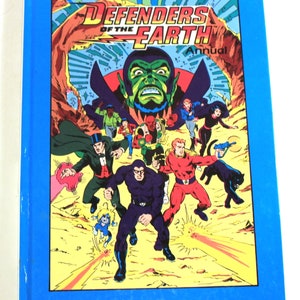 May include: A blue book cover with the title "Defenders of the Earth Annual" in yellow and red lettering. The cover features a comic book style illustration of a group of superheroes fighting a villain.